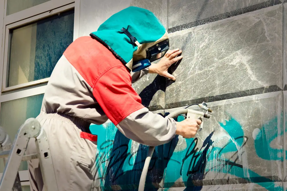 Reinigungskraft entfernt mit Sandstrahler Graffiti